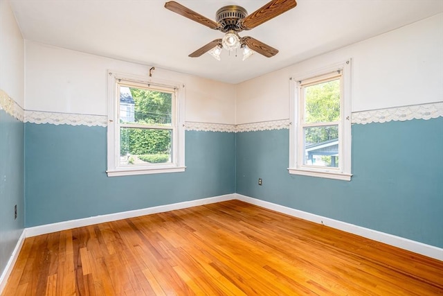 unfurnished room featuring plenty of natural light, hardwood / wood-style floors, a ceiling fan, and baseboards