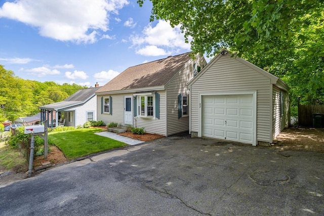 new england style home featuring a garage, driveway, a front yard, and an outbuilding