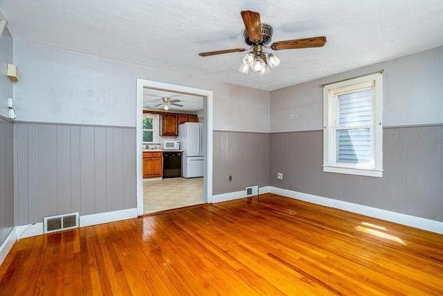 spare room featuring a wainscoted wall, ceiling fan, light wood finished floors, wood walls, and baseboards