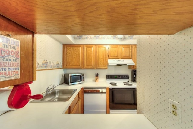 kitchen featuring white appliances, under cabinet range hood, a sink, wallpapered walls, and light countertops