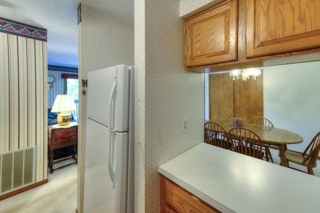kitchen featuring freestanding refrigerator, wallpapered walls, brown cabinets, light countertops, and light carpet