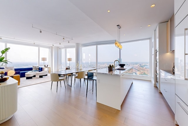 kitchen with white cabinets, hanging light fixtures, a center island with sink, a breakfast bar, and sink