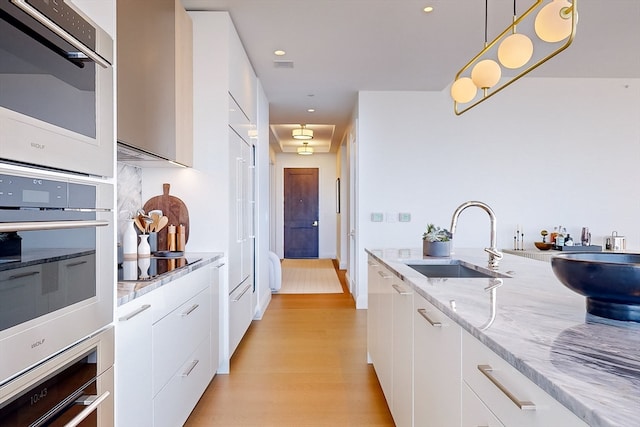 kitchen with black electric cooktop, sink, decorative light fixtures, light wood-type flooring, and white cabinets