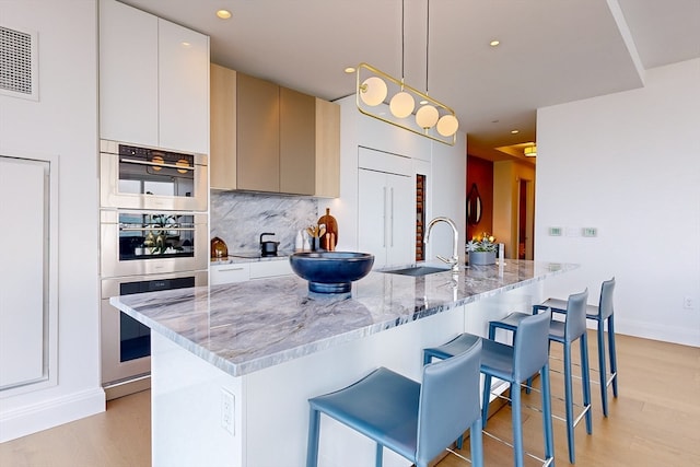 kitchen with hanging light fixtures, a breakfast bar, light hardwood / wood-style flooring, sink, and light stone counters