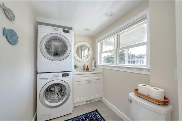 laundry area featuring light tile patterned floors, baseboards, a sink, stacked washer and clothes dryer, and cabinet space