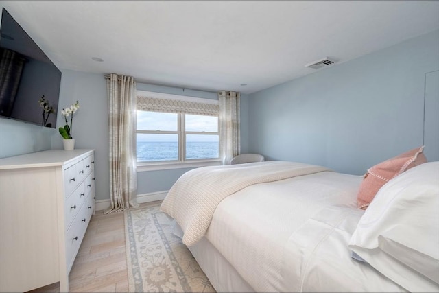 bedroom featuring a water view, baseboards, visible vents, and light wood-style floors