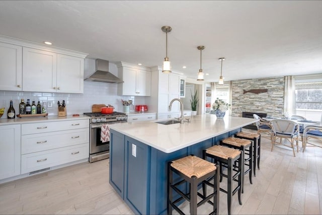 kitchen featuring light wood-style flooring, stainless steel gas range, a sink, white cabinetry, and wall chimney exhaust hood