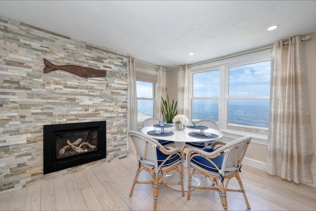 dining room with wood finished floors, recessed lighting, a water view, baseboards, and a stone fireplace