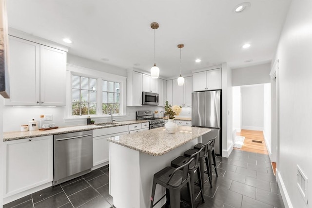 kitchen featuring stainless steel appliances, white cabinetry, hanging light fixtures, and light stone counters