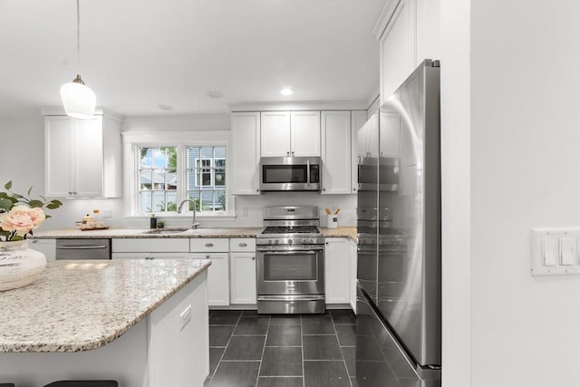 kitchen with appliances with stainless steel finishes, white cabinetry, sink, hanging light fixtures, and light stone counters