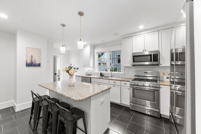 kitchen featuring white cabinetry, light stone counters, decorative light fixtures, a center island, and appliances with stainless steel finishes