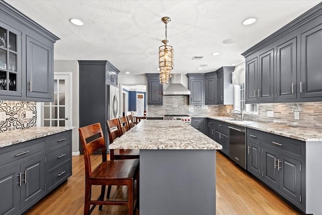 kitchen featuring hanging light fixtures, wall chimney range hood, a center island, a kitchen bar, and glass insert cabinets