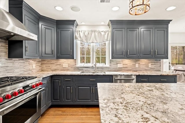 kitchen featuring light stone counters, high end stainless steel range oven, wall chimney range hood, and a sink