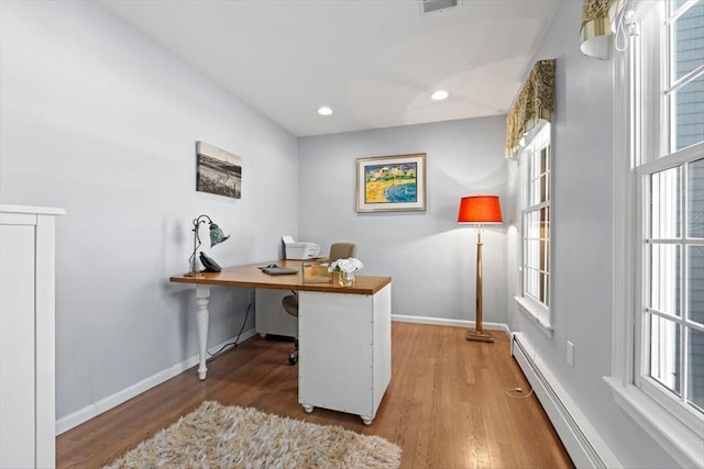 office space with plenty of natural light, a baseboard heating unit, and wood finished floors