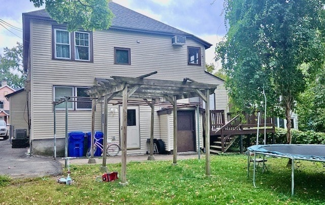 rear view of house featuring a trampoline, a deck, a pergola, central air condition unit, and a yard