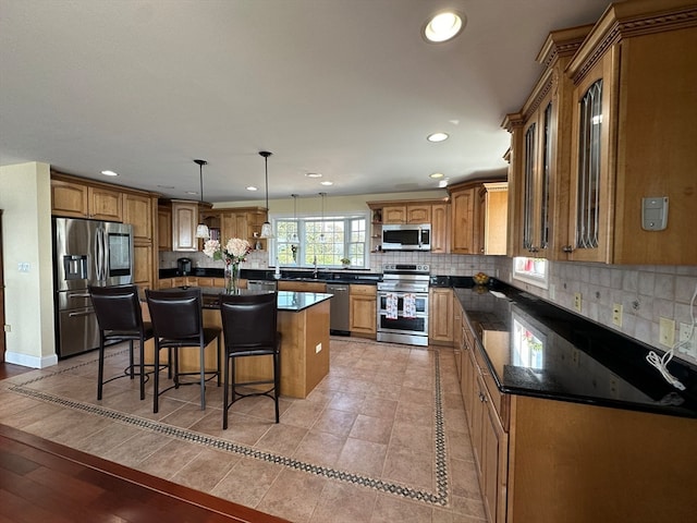 kitchen featuring a kitchen island, pendant lighting, appliances with stainless steel finishes, tasteful backsplash, and light wood-type flooring