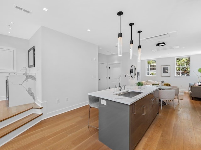 kitchen featuring light hardwood / wood-style floors, a kitchen bar, sink, a kitchen island with sink, and hanging light fixtures