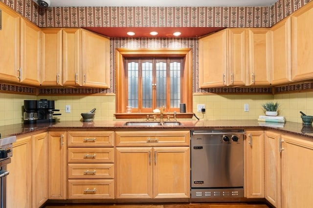 kitchen with stainless steel dishwasher, decorative backsplash, light brown cabinetry, a sink, and dark stone countertops