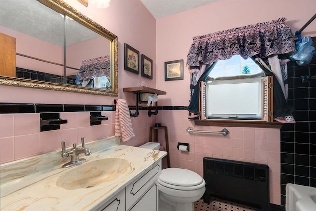 bathroom with wainscoting, vanity, toilet, radiator, and tile walls
