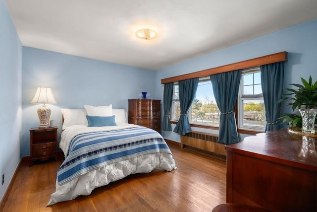 bedroom featuring radiator heating unit, baseboards, and wood finished floors