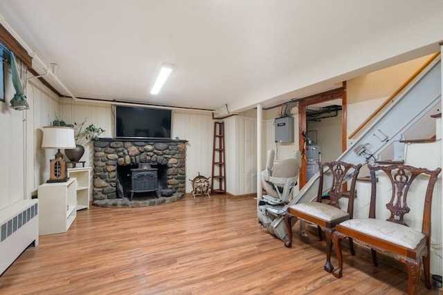living area with electric panel, water heater, a wood stove, light wood-type flooring, and radiator heating unit