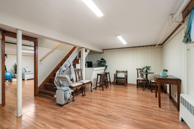 finished below grade area with radiator heating unit, stairway, and light wood-type flooring