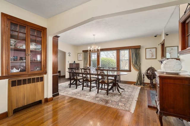 dining room with an inviting chandelier, radiator, baseboards, and wood finished floors
