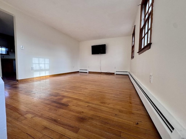 unfurnished living room featuring baseboard heating and wood-type flooring