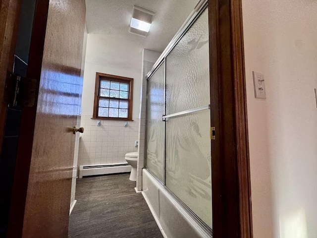 bathroom with toilet, combined bath / shower with glass door, tile walls, a baseboard heating unit, and wood-type flooring