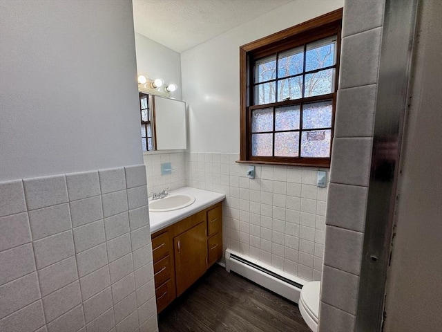 bathroom with tile walls, hardwood / wood-style flooring, toilet, a baseboard radiator, and vanity