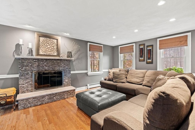 living room featuring recessed lighting, baseboard heating, a glass covered fireplace, wood finished floors, and baseboards