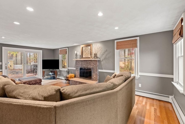 living area with a wealth of natural light, baseboard heating, a glass covered fireplace, and light wood-style flooring