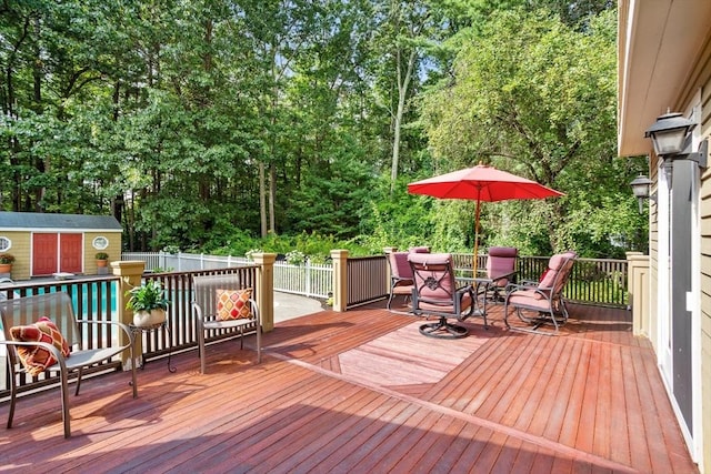 wooden terrace featuring a storage unit, fence, outdoor dining area, and an outbuilding