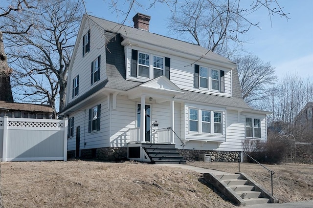 view of front of property featuring a gambrel roof, a chimney, and fence