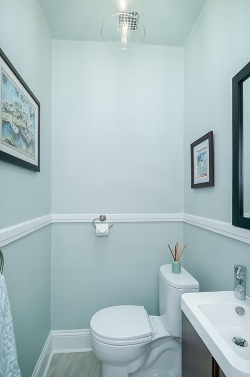 half bath with a sink, baseboards, toilet, and wood finished floors