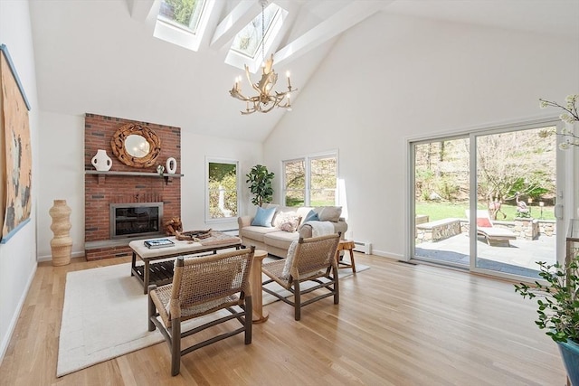 living area with a fireplace, high vaulted ceiling, a chandelier, light wood-style flooring, and a skylight
