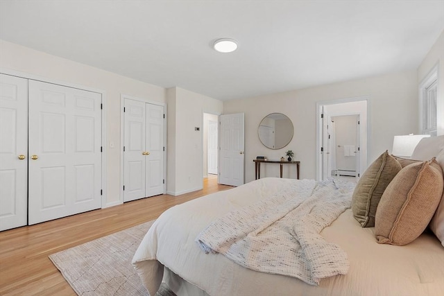 bedroom with a baseboard radiator, two closets, wood finished floors, and connected bathroom