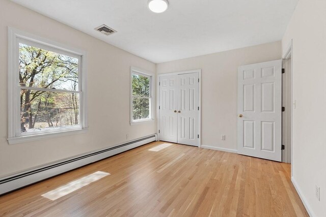 unfurnished bedroom with visible vents, baseboard heating, baseboards, a closet, and light wood finished floors