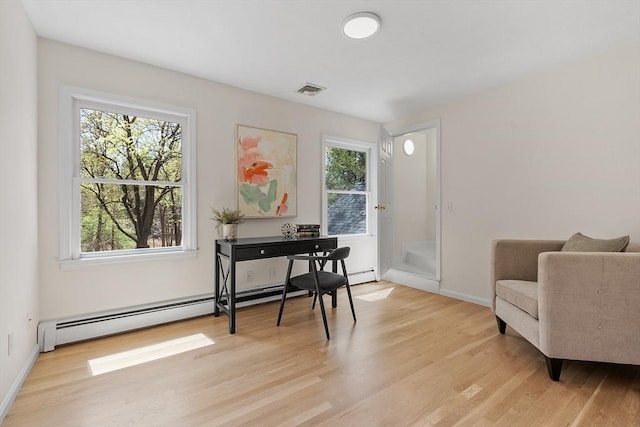 living area featuring light wood-style floors, baseboards, a baseboard heating unit, and visible vents