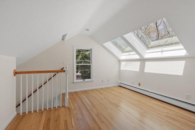 additional living space with baseboards, a baseboard heating unit, lofted ceiling with skylight, and wood finished floors