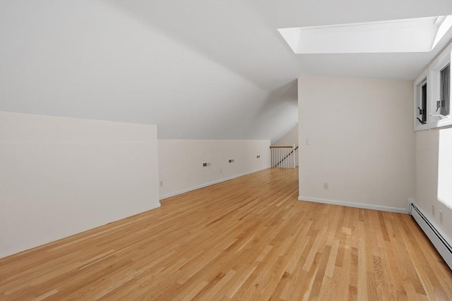 bonus room with light wood-type flooring, a baseboard radiator, baseboards, and vaulted ceiling with skylight