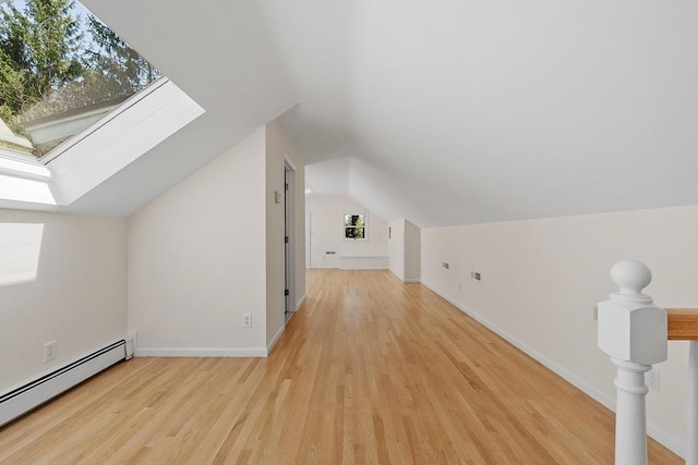 additional living space with light wood-type flooring, baseboards, lofted ceiling with skylight, and baseboard heating