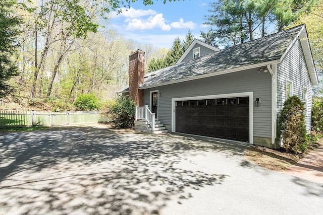 view of side of home featuring fence, a chimney, driveway, and a garage