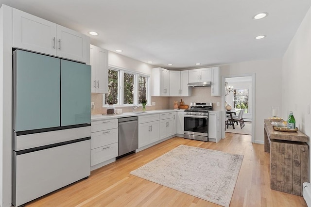 kitchen with under cabinet range hood, stainless steel appliances, white cabinetry, and backsplash