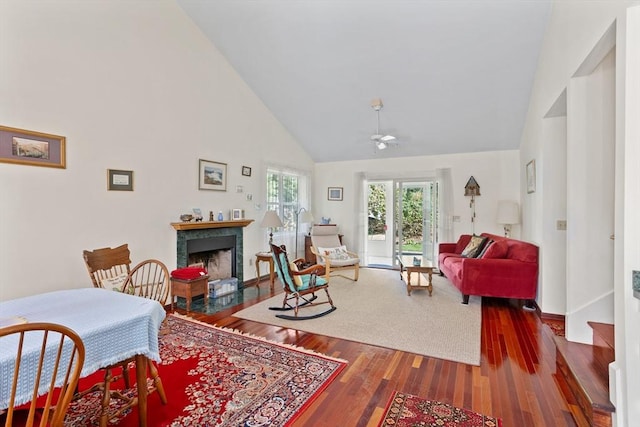 living room featuring baseboards, a fireplace, wood finished floors, high vaulted ceiling, and a ceiling fan