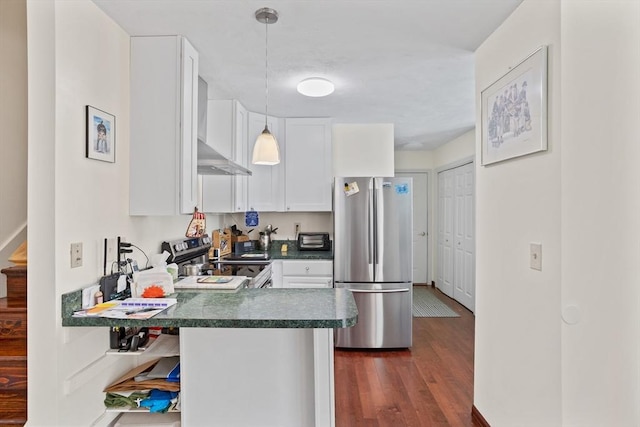 kitchen with dark countertops, dark wood finished floors, appliances with stainless steel finishes, wall chimney exhaust hood, and white cabinets