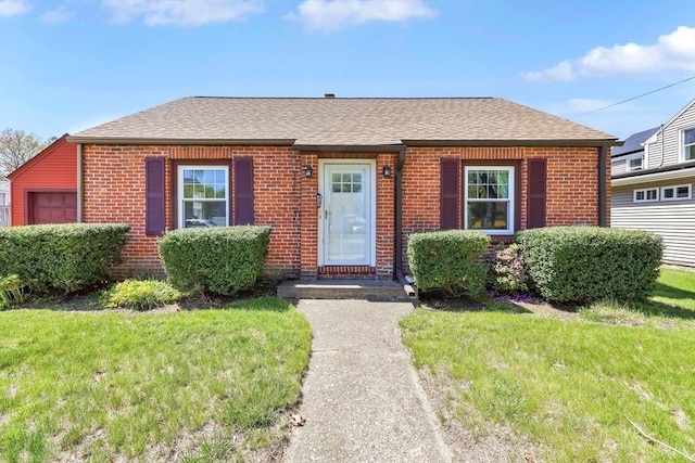 bungalow with roof with shingles, a front yard, and brick siding