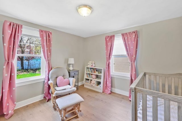 bedroom with a nursery area, baseboards, and wood finished floors