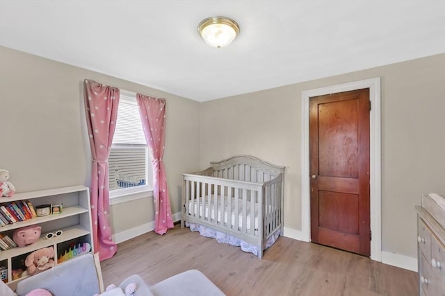 bedroom featuring baseboards, a nursery area, and wood finished floors