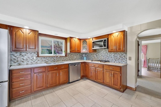 kitchen featuring light countertops, brown cabinets, a sink, backsplash, and stainless steel appliances